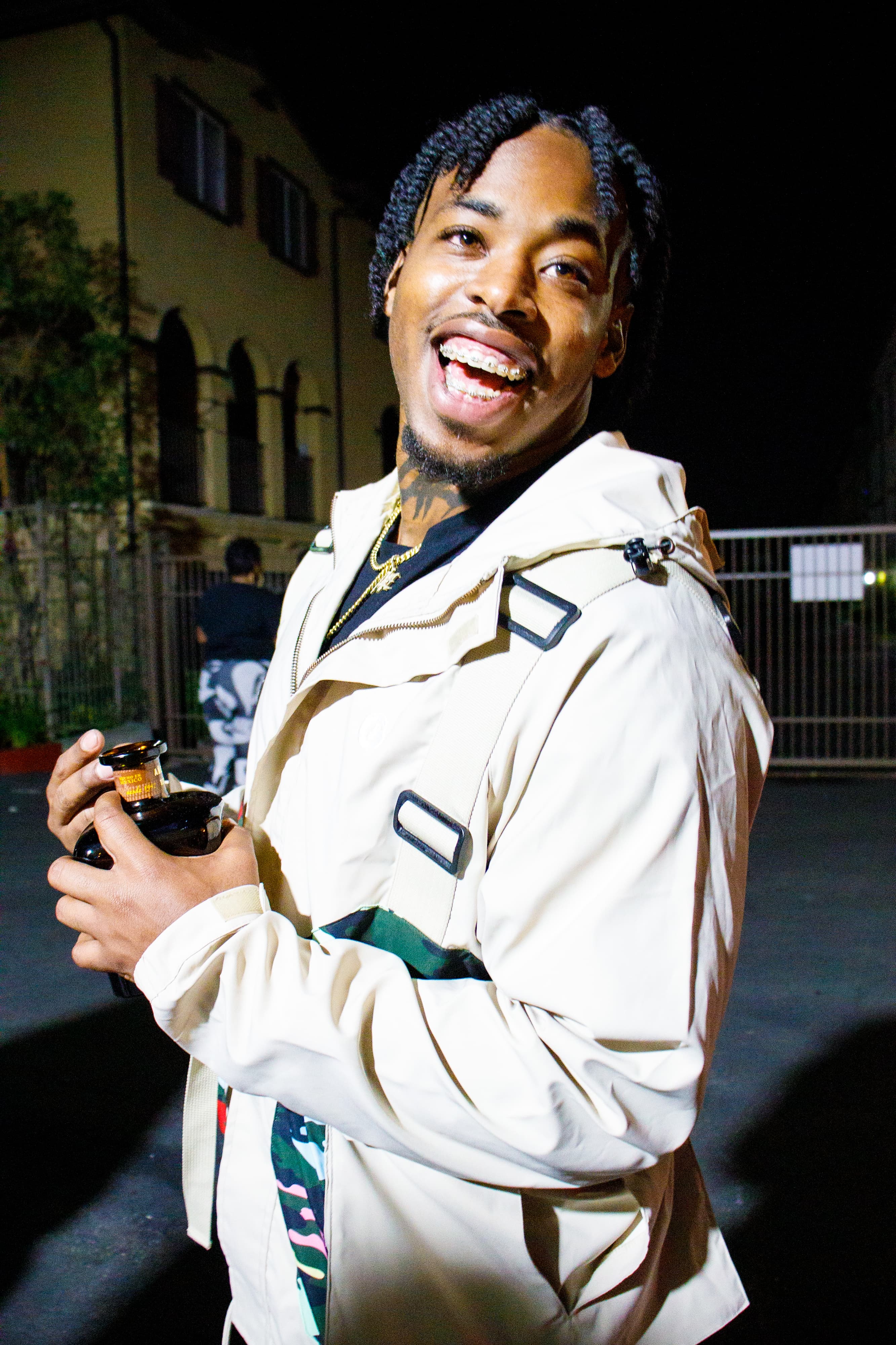 1TakeQuan laughing in a cream jacket at night